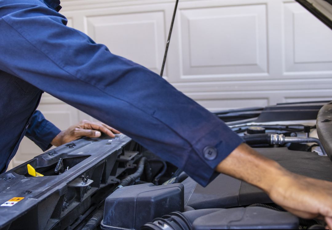 Foto ilustrativa de stock: un mecánico revisa el motor de un carro frente a un garaje residencial (no es Jorge)